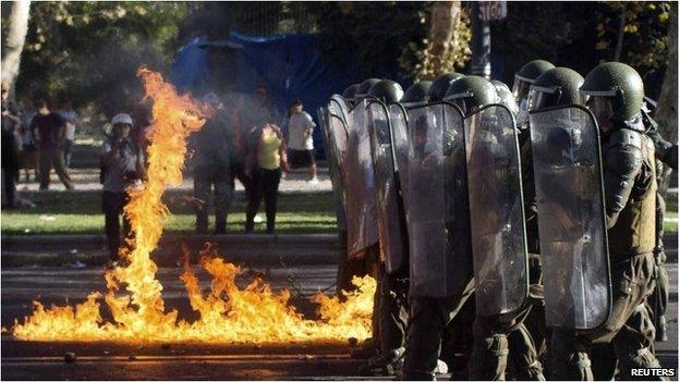 Riot troops march past fire from petrol bomb