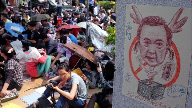 Student protesters sit next to a caricature poster of Taiwan's President Ma Ying-jeou as ongoing protests against a trade agreement with mainland China continue at the parliament in Taipei on 25 March 2014