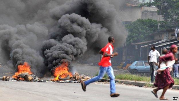 A woman carrying her child runs past supporters of Alassane Dramane Ouattara burning tyres on a street of Abidjan, on 24 February 2011