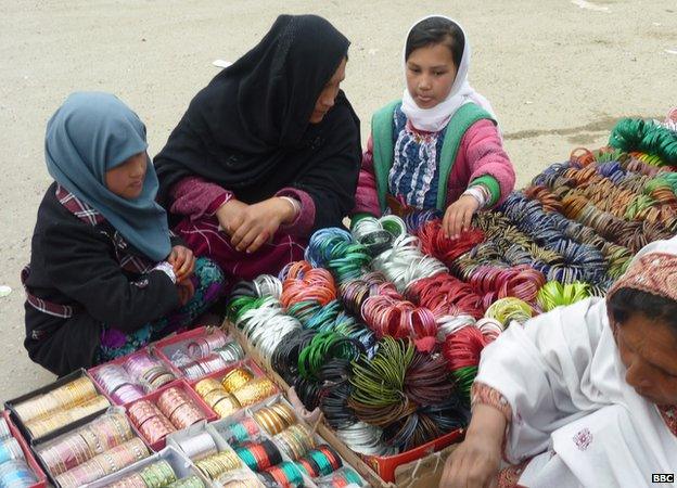 A woman and two young girls browse a stall selling brightly coloured bangles