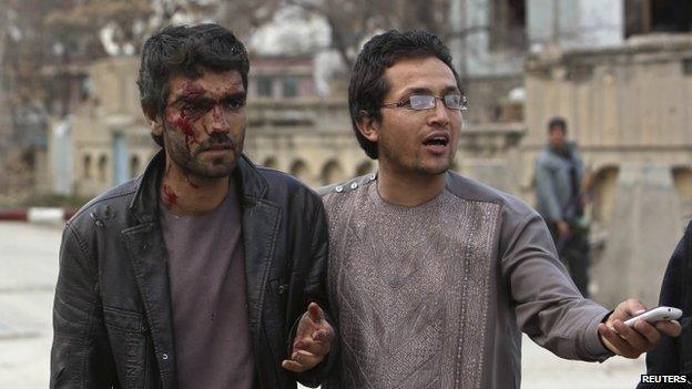 An Afghan man helps an injured man at the site of the attack in Kabul