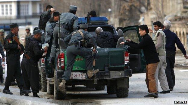 Afghan policeman evacuate foreigners from a guest house, the site of an attack, in Kabul (28 March 2014)