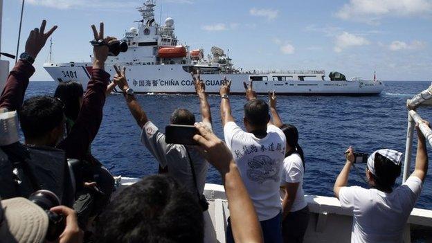 Philippine Marines and a local television reporter (L) gesture towards a Chinese Coast Guard vessel in the South China Sea March 29,