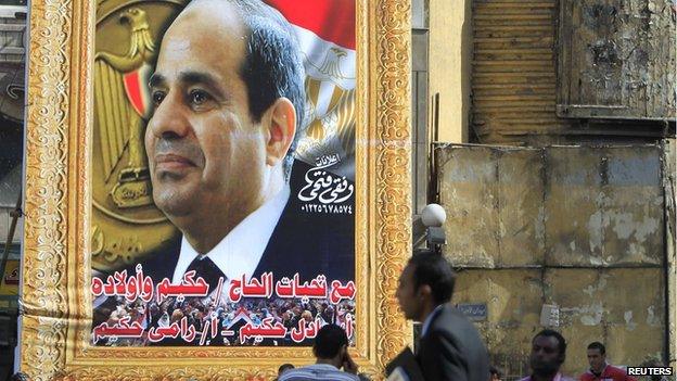 People walk past a banner for Egypt's army chief Field Marshal Abdel Fattah al-Sisi in downtown Cairo on 26 March 2014.