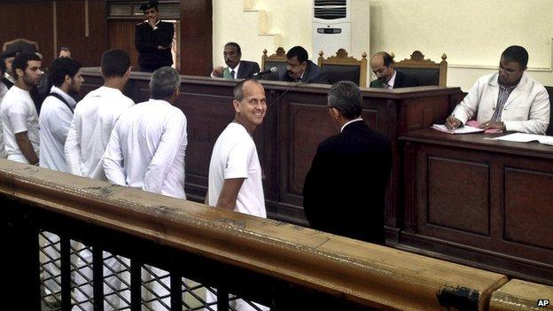 Al-Jazeera English correspondent Peter Greste, second right, smiles as he and bureau chief Mohamed Fahmy and producer Baher Mohamed stand in a courtroom along with several other defendants during their trial on terror charges, in Cairo, Egypt on 31 March 2014.