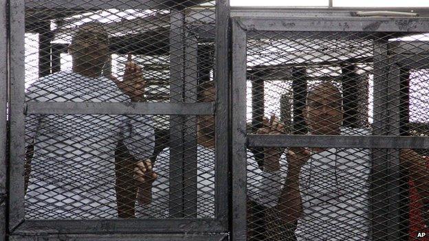 Al-Jazeera English bureau chief Mohammed Fahmy, left, producer Baher Mohamed, centre, and correspondent Peter Greste, right, appear in a defendant's cage in a courtroom along with several other defendants during their trial on terror charges, in Cairo, Egypt, on 31 March 2014.