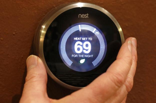 A hand is on the Nest smart heating thermostat