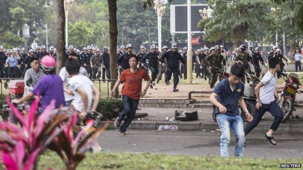 People run as riot police officers (back) try to disperse protesters against a chemical plant project in Maoming, Guangdong province, on 31 March 2014