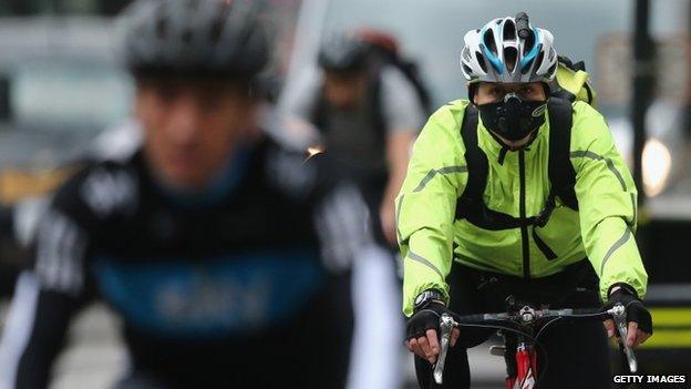 A woman riding a bicycle while wearing a mask over her mouth and nose