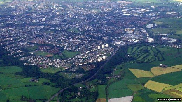 Looking along the A725 from Hamilton. The course if the former railway line from Hamilton to East Kilbride can be seen to the left of the white field near the bottom of the photo.