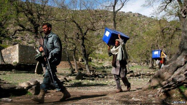 Afghan policeman walks with election workers carrying ballot boxes in Darenoor, Nangarhar province, on 4 April 2014