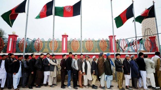 Afghan residents wishing to vote line up underneath underneath Afghan flags outside a polling station in Mazar-i-Sharif