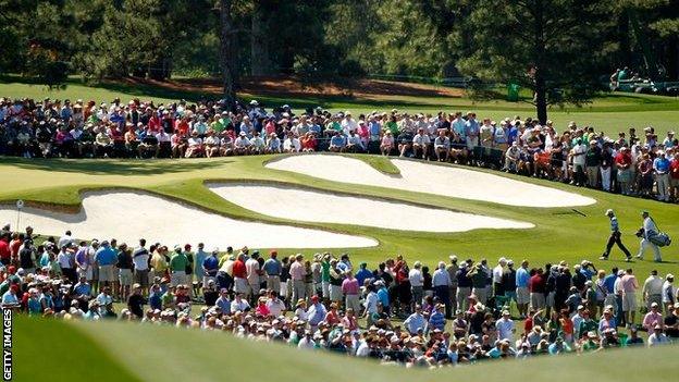 Spectators watch as Charl Schwartzel and his caddie Greg Hearmon walk up the seventh hole at Augusta