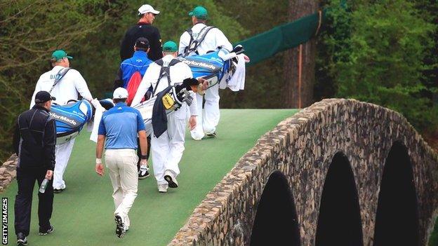 The caddies of Mike Weir, Garrick Porteous and Jason Day walk over Hogan's Bridge on the 12th hole during practice