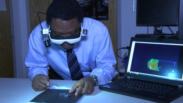 Dr Samuel Achilefu looks a vial containing the dye, whilst an image of what he see is projected on a computer screen beside him.