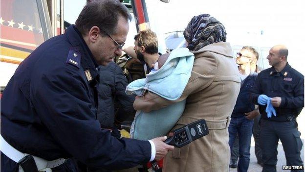 An Italian police officer checks a migrant in the Sicilian harbour of Augusta April 9