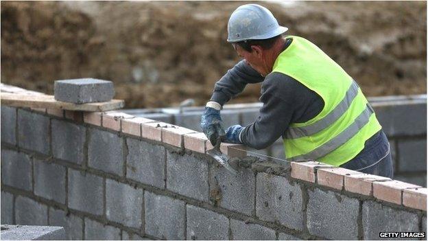 A builder adding bricks to the wall of a house which is being built