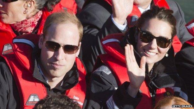 The duke and duchess smile and wave from the jet boat