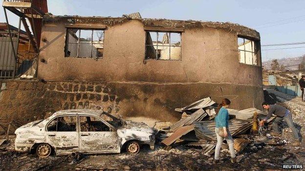 Residents survey the damage after a forest fire burned homes in Valparaiso, April 13, 2014.