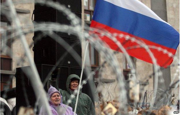 Pro-Russia activists wave a Russian flag and shout slogans behind a razor wire-topped barricade outside the regional government building in Donetsk