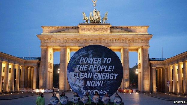 Members of environmental activist group Greenpeace pose with a giant placard which reads "Power to the people! Clean energy now" in front of the Brandenburg Gate in Berlin April 13