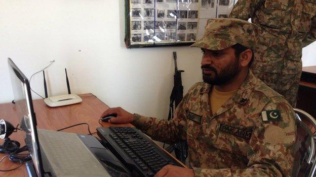 An army officer works at a checkpoint with a list of suspected militants on the wall