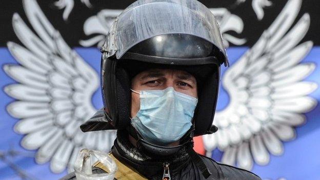 An armed pro-Russian activist stands in front of seized the Ukrainian regional administration building in the eastern Ukrainian town of Sloviansk, Ukraine, on Monday 14 April 2014, with the Russian national sign in the background