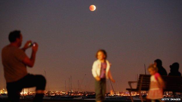 A man takes a photo of his children as the "Blood Moon" rises over the water in Wlliamstown in Melbourne, Australia, 15 April 2014