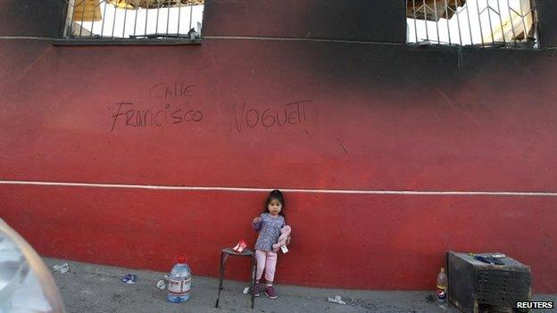 A girl stands in front of a wall of a burned house during the fire that affected several neighbourhoods on the hills in Valparaiso on 14 April 2014