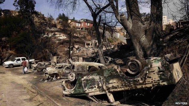 A resident walks past cars destroyed by a major fire in Valparaiso (13 April 2014)