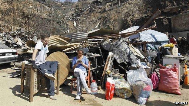 Residents sit with belongings in front of remains of houses after a fire burned several neighbourhoods in the hills in Valparaiso on 14 April 2014