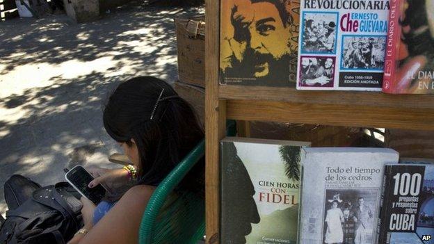 A street vendor plays with her smartphone while selling books about the Cuban revolution