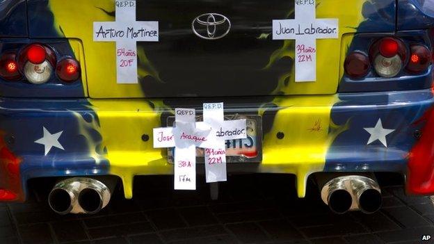 Several crosses with the names of people killed during the protests hang in a car decorated with the Venezuelan flag during a march of remembrance for those fallen during the protests, in Caracas, Venezuela, Tuesday, April. 15, 2014.