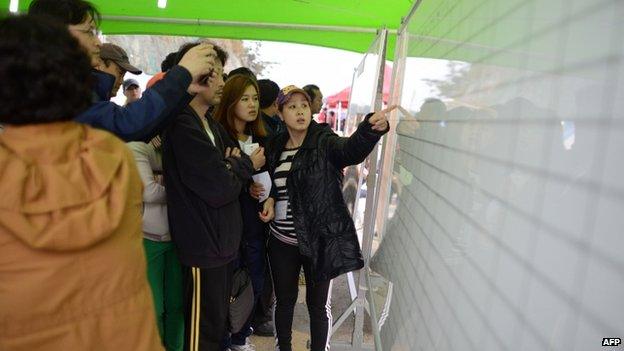 Relatives look at the names of recovered victims of the South Korean ferry "Sewol" at on a display board at Jindo harbour on April 20, 2014