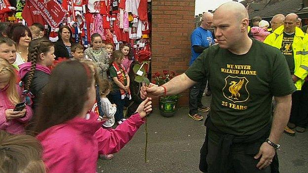 A walker hands a red rose to a child at the Anfield memorial