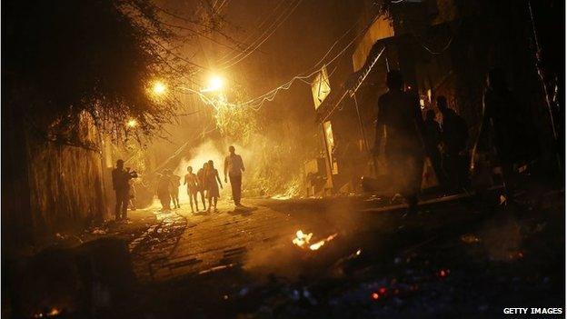 People walk through smoke from fires set by protesters following shootings in the pacified Pavao-Pavaozinho community, just blocks from Copacabana Beach on 22 April, 2014