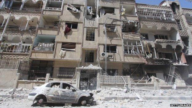 A damaged car next to damaged buildings in Al-Maliha town, in the suburbs of Damascus