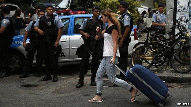 A tourist walks as police officers guard the entrance of the Pavao-Pavaozinho neighbourhood in Rio de Janeiro on 23 April, 2014
