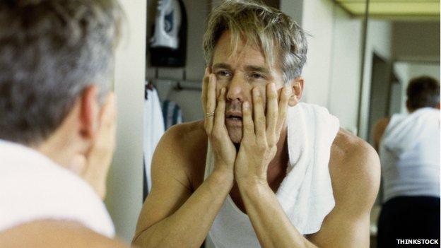 A tired-looking man man looking in the mirror