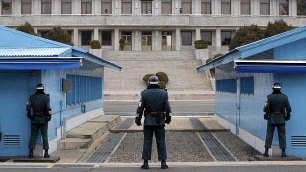 A North Korean soldier looks at the southern side as three South Korean soldiers guard at the border village of Panmunjom (South Korean side) on 12 March 2014.