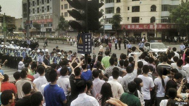 Workers protest during a strike as police stand guard at a crossroads near the factory area of Yue Yuen Industrial, in Dongguan, Guangdong province (18 April 2014)