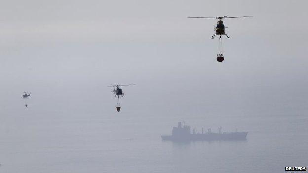 Helicopters pick up water from the Pacific Ocean to dump on the smouldering remains of houses after a fire burned several neighbourhoods in the hills in Valparaiso city on 14 April, 2014.