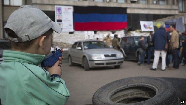 A boy points a toy gun as a group of journalists stand in front of Sloviansk's town hall (28 April 2014)