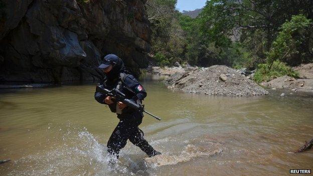 A federal police officer crosses a river on the outskirts of Arteaga during a search for Knights Templar leader Servando Gomez (26 April 2014)