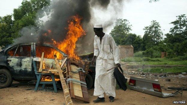 A man stands near a vehicle and other belongings set on fire by its owners who did not want to leave them behind for looters in Bangui, Car (27 April 2014)