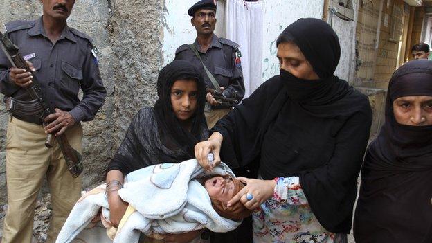 Pakistani policemen stand guard as a health worker gives a child a polio vaccine in Karachi, Pakistan, on 9 March 2014.