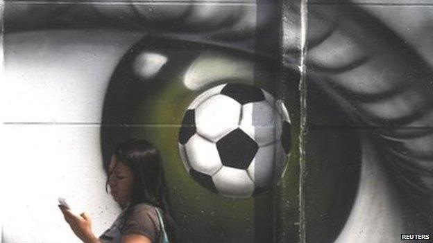 A woman walks past a graffiti of an eye and a soccer ball in Sao Paulo