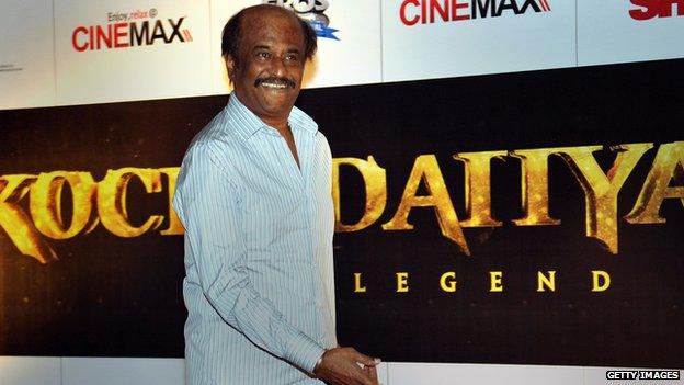 Rajinikanth in front of a poster for his new film