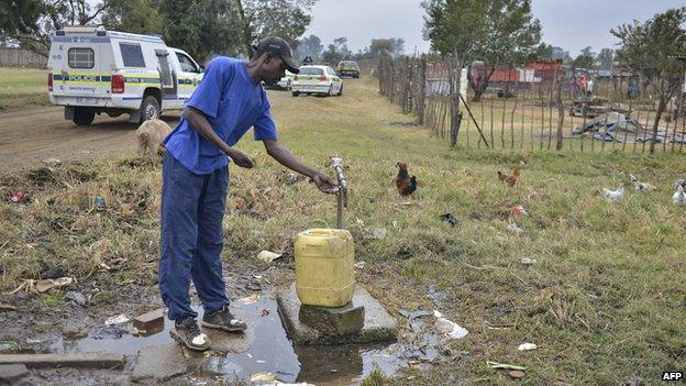 A man takes water while South African police officers patrol aboard vehicles in the restive township of Gugulethu