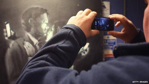 A mobile phone is used to take a picture of Banksy's Mobile Lovers artwork